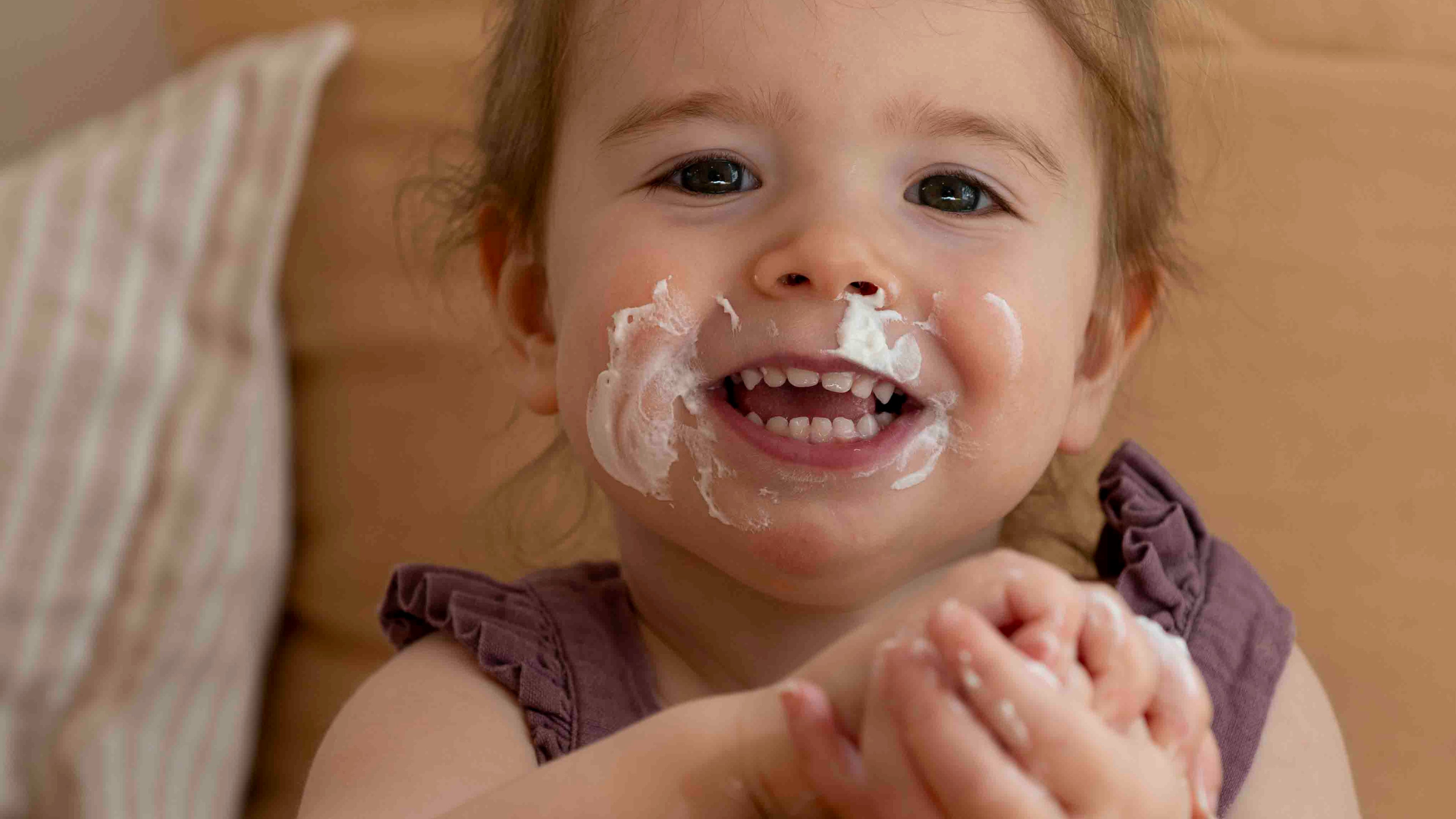 Child with yohurt on face and hands, smiling